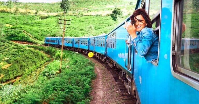 Happy young woman with with her head sticking out the window of a blue train | solo travel quotes about traveling alone