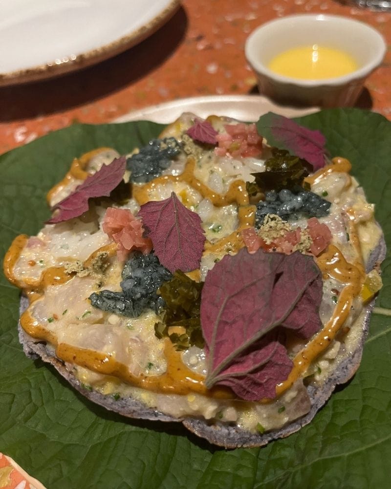 Tostada topped with raw fish, sauces and purple leaves on a large green leaf at Esquina Común in Mexico City