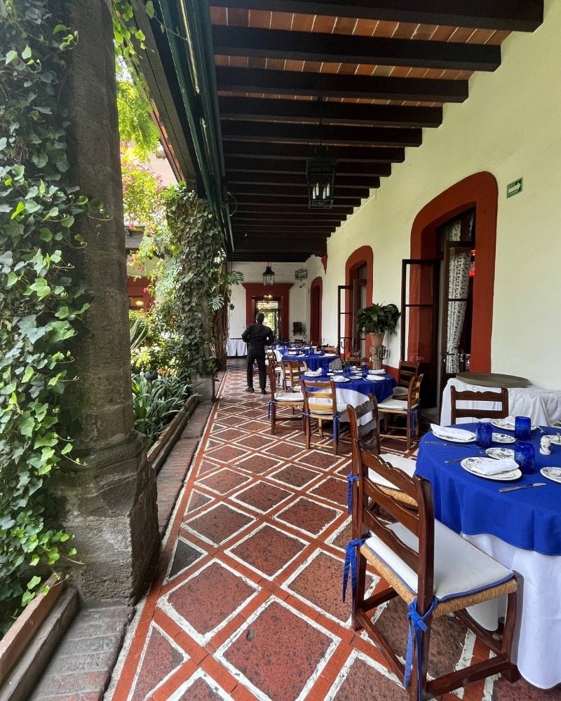 Covered terrace with blue tablecloths and a red tile floor at San Ángel Inn in Mexico City