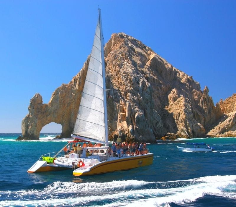 catamaran sailboat near large rocks in the ocean | things to do in cabo mexico