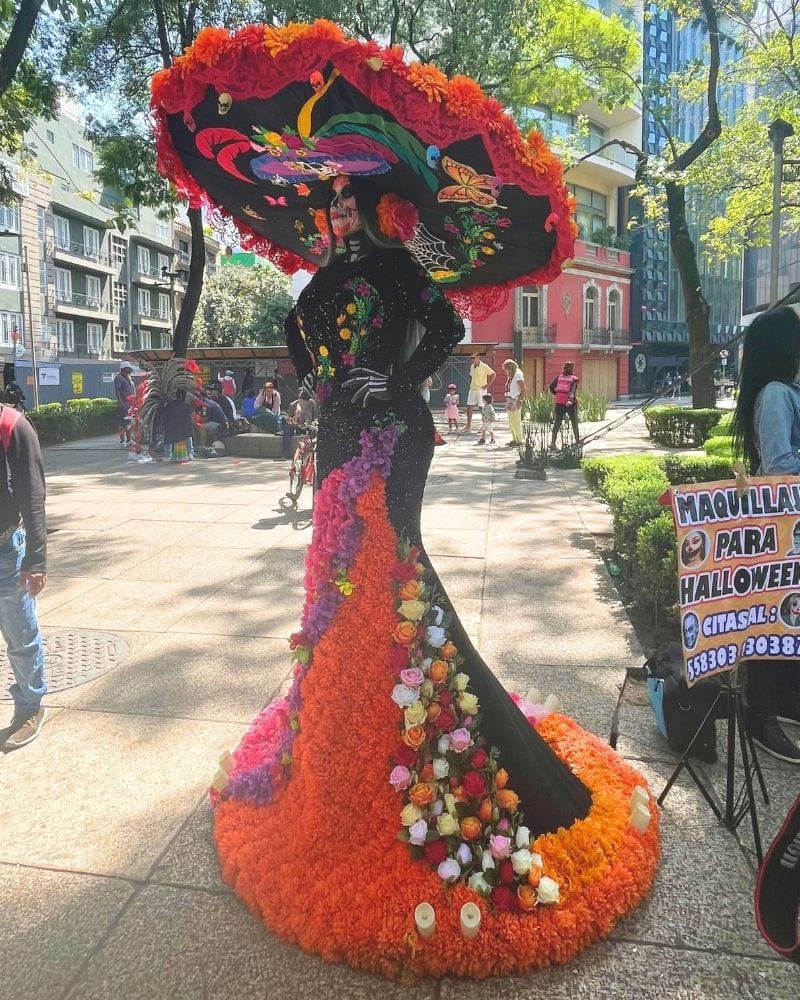 La Catrina costume with a giant floral hat and a gown covered in orange flowers on a Mexico City street for Day of the Dead
