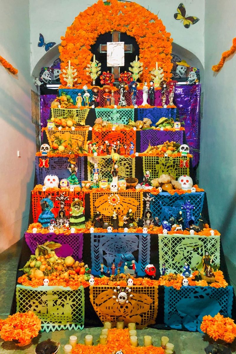 Tiered Day of the Dead altar with a marigold arch, candles and papel picado