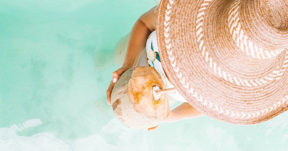 woman in straw hat drinking from a coconut in the pool