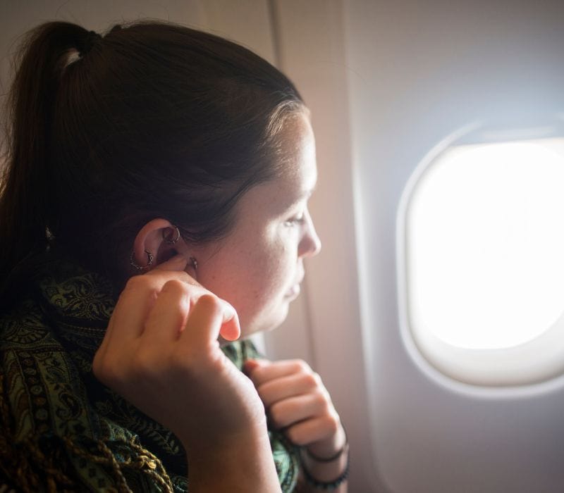 woman on a flight putting on earplugs