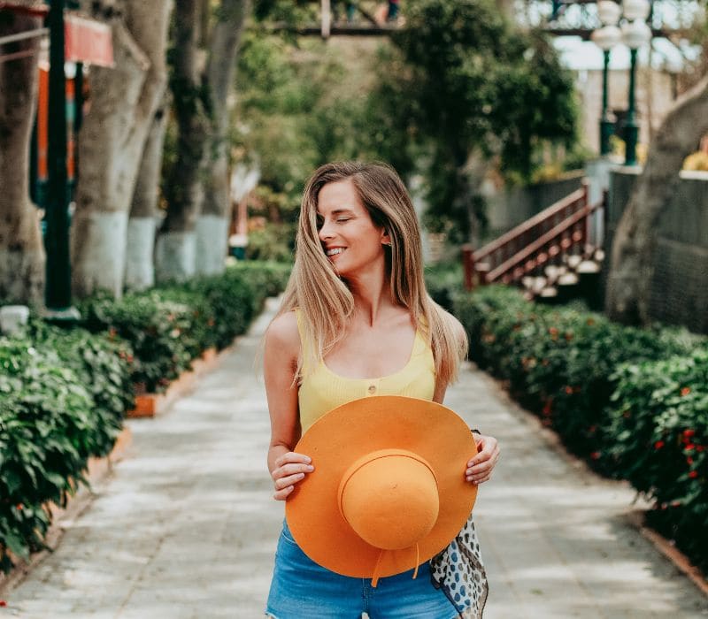 woman wearing short jeans and sleeveless yellow top holding a sunhat