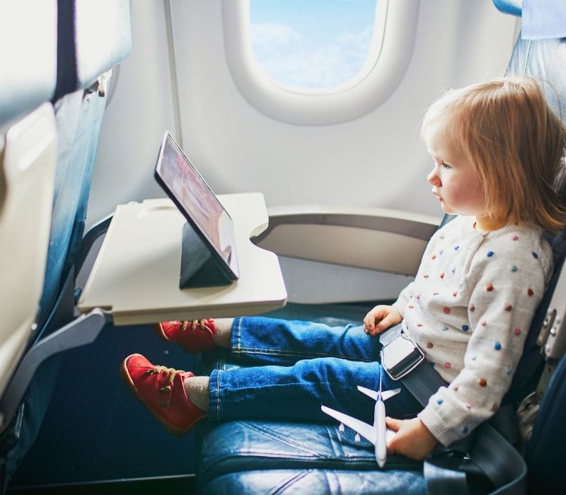 toddler holding a toy airplane while watching a show on an ipad
