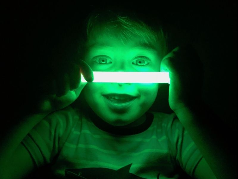 little kid holding a green glow stick up to their face