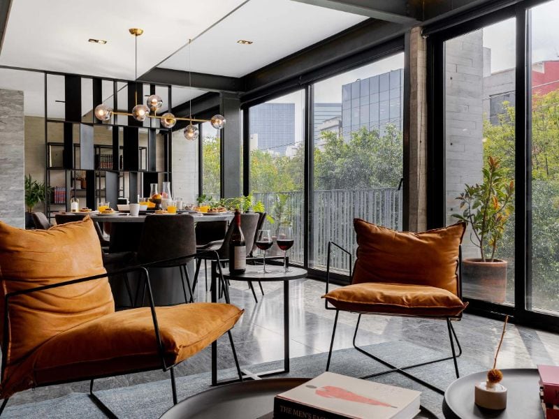 Glass-walled living room with orange armchairs at the 3-Bedroom Polanco Apartment by Masaryk, a luxury Airbnb in Mexico City