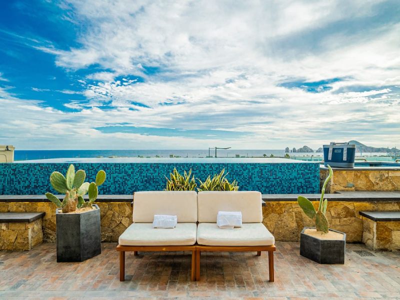 Private terrace with lounge chairs and an infinity pool overlooking the ocean at the 3-bedroom Vista Vela condo, a Cabo Airbnb in El Tezal