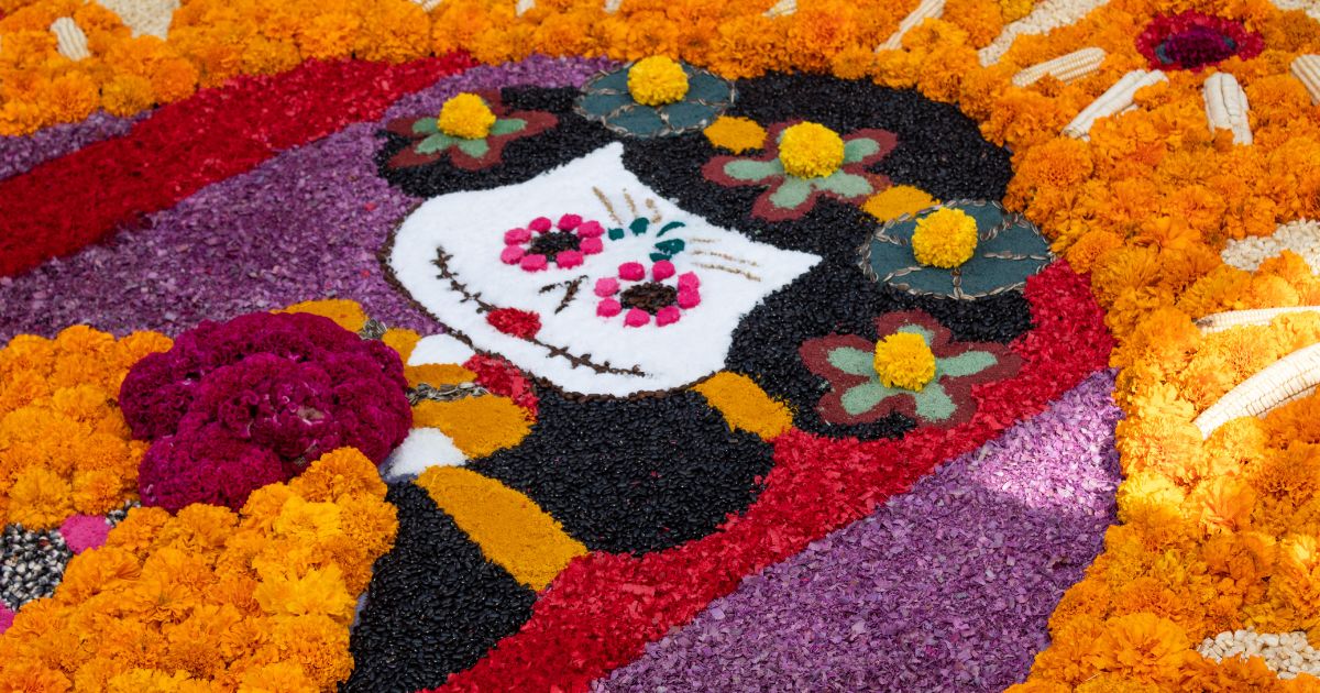 Colorful carpet of marigolds and dyed sawdust showing a decorated skull face for Day of the Dead