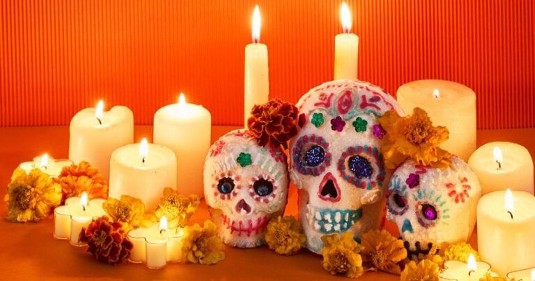 Decorated sugar skulls, lit white candles and orange marigolds on an orange table for Day of the Dead