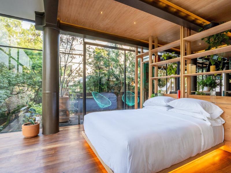 Loft bedroom with floor-to-ceiling windows and plants at the vintage loft Airbnb in Condesa, Mexico City
