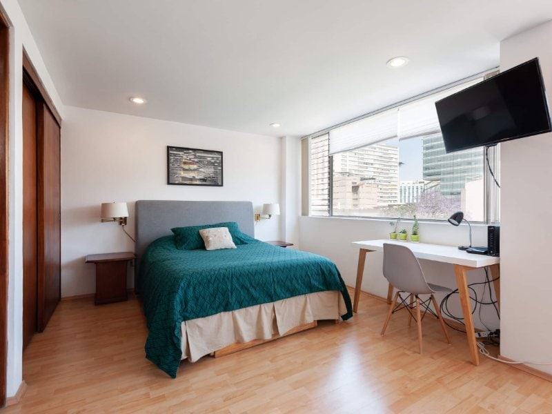 Queen bed with a green cover and desk by the window at the Bright Studio in Nápoles, Mexico City