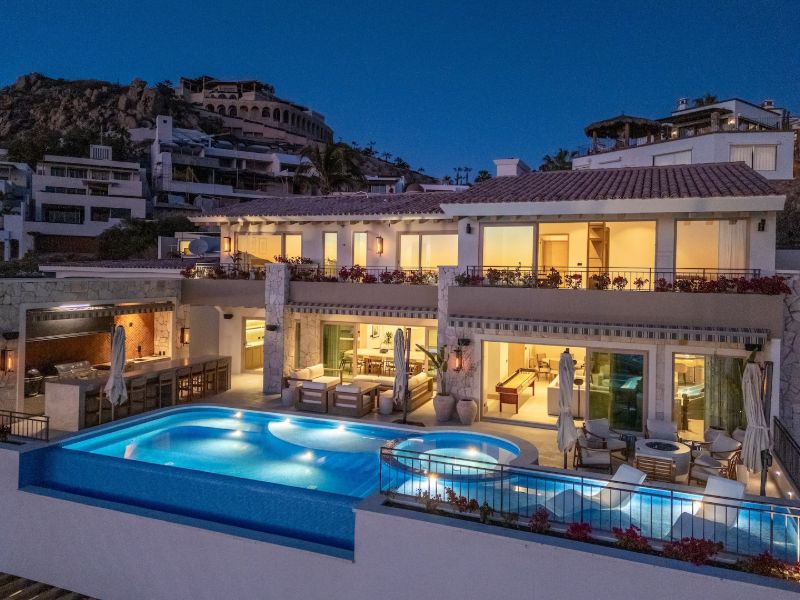 Casa La Maraca and its infinity pool lit up at dusk in Pedregal, Cabo San Lucas