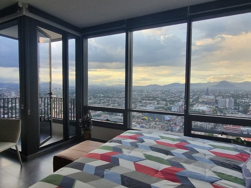 Bedroom with floor-to-ceiling city views at the Be Grand Reforma loft Airbnb, Mexico City