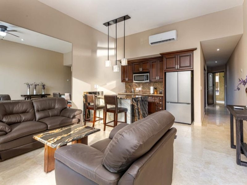 Living room with leather sofas and an open kitchen at the Ocean-View Condo in Cabo Bello, Cabo San Lucas