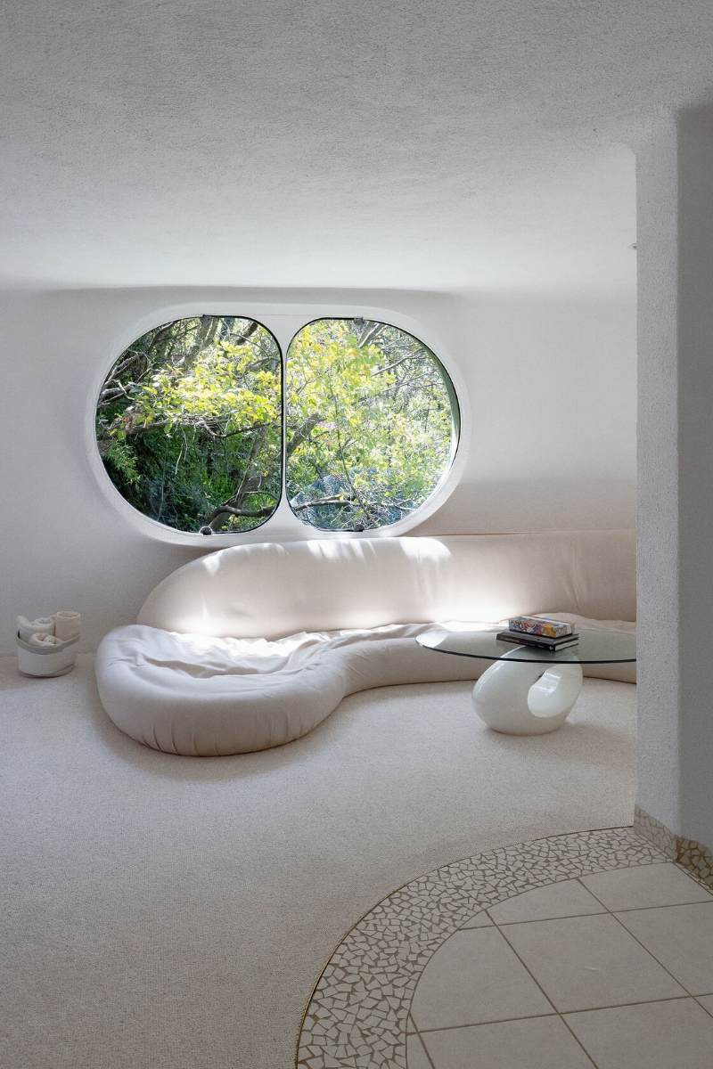 Snake house living room with a curved white sofa under a large oval window