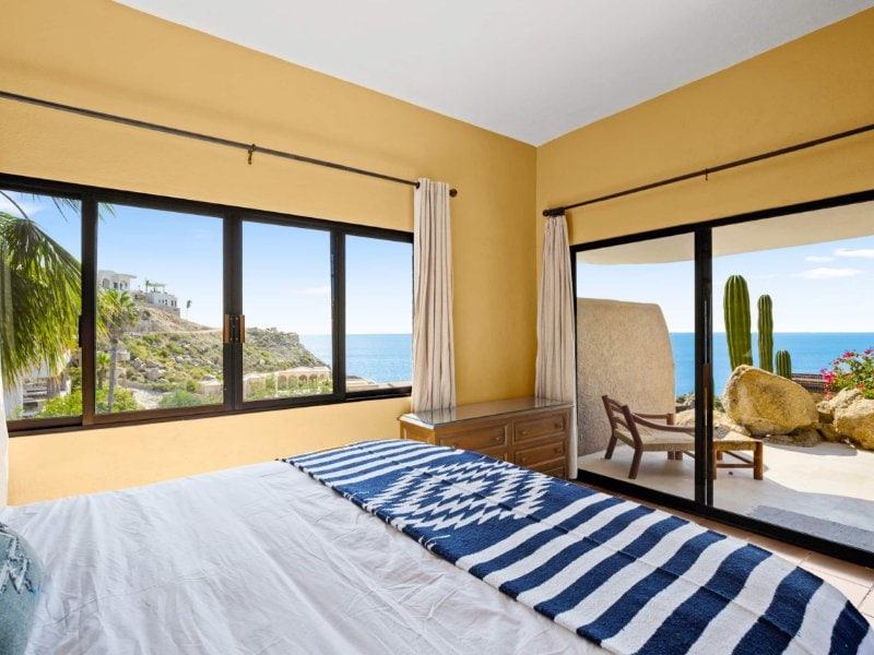 Bedroom with a striped bedspread and ocean-view windows at Villa Isla in Pedregal, Cabo San Lucas